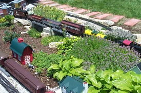 This shot  was taken from the same position as the previous photo; Wil just rotate about 65 degrees to the right.  You can see part of our New Boston community in the upper left corner.  The barn structures are a trashbashed Fischer Price Cape Cod and a North States barn bird feeder.  Aristo heavyweights are resting on the passing siding at the 'back' of the railroad, from the typical visitor's point of view.  Click for bigger photo.