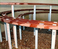 This photo shows the Bondo as it has been applied to fill the screw-holes in the roadbed, including the screws that hold the verticle PVC piping in place. Click for bigger photo.